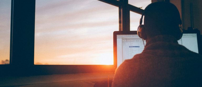 Person mit Kopfhörern arbeitet am Computer bei Sonnenuntergang.